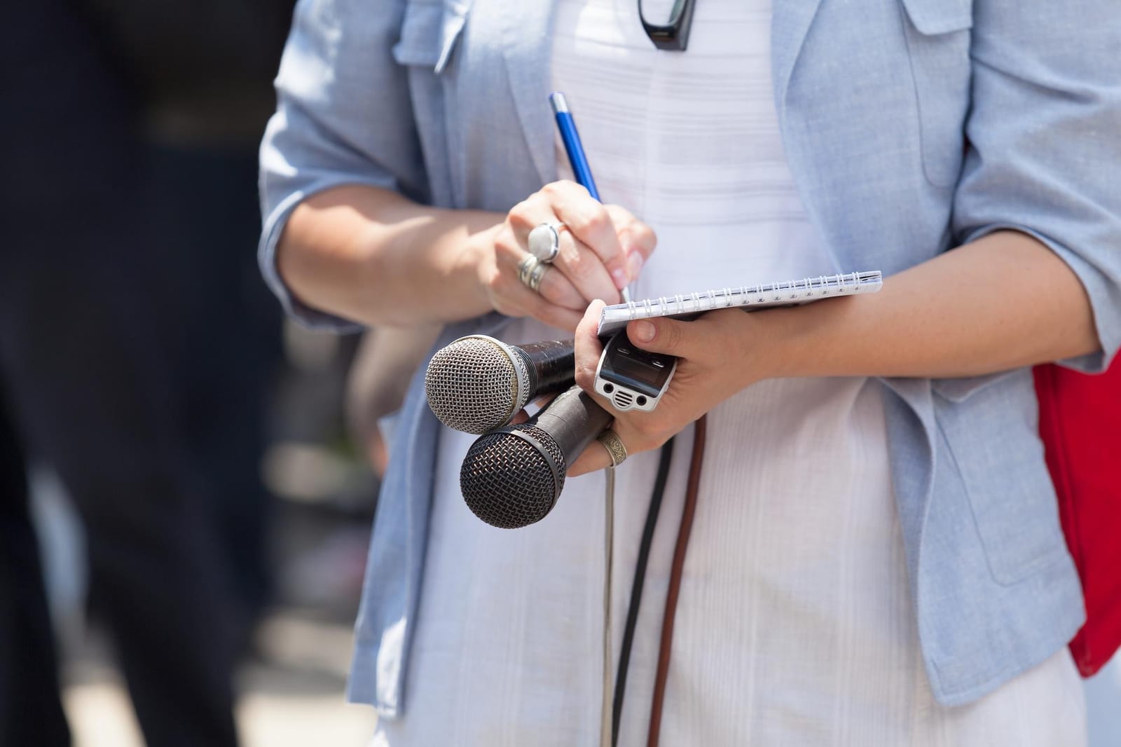 A Fiddlehead Press journalist taking notes while holding a microphone during an interview.